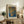 May include: Framed art print with dotted abstract pattern in blue, orange and green tones displayed on rustic wooden sideboard. Room setting shows fern plant, ceramic vase, stacked books, and beige upholstered chair. Print features Japanese text and polka dot infinity net design in earth tone color palette within natural wood frame.