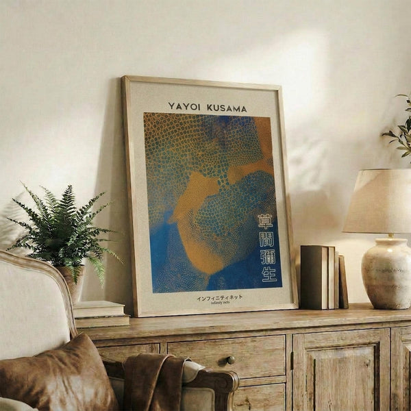 May include: Framed art print with dotted abstract pattern in blue, orange and green tones displayed on rustic wooden sideboard. Room setting shows fern plant, ceramic vase, stacked books, and beige upholstered chair. Print features Japanese text and polka dot infinity net design in earth tone color palette within natural wood frame.