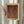 May include: Framed art print with warm orange and brown abstract textural pattern, resembling organic or cellular forms with deep burgundy accents. Artist name displayed at bottom in bold black text. Light wood frame mounted on neutral wall beside dried pampas grass stems, creating soft shadows in natural lighting.