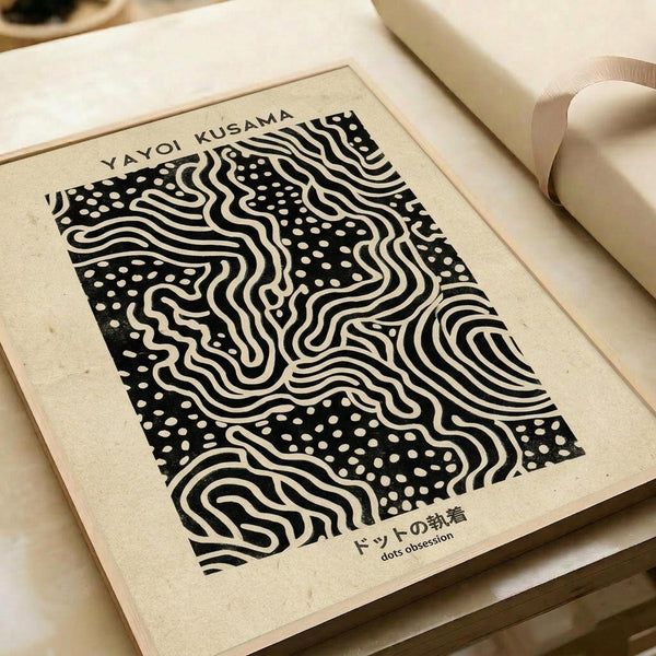 Black and white abstract art print with flowing wavy lines and scattered dots creating an optical illusion pattern, displayed in a light wood frame on cream-colored paper. The artwork sits on white paper with a beige ribbon visible in the corner, showing Japanese text at the bottom that reads "dots obsession."