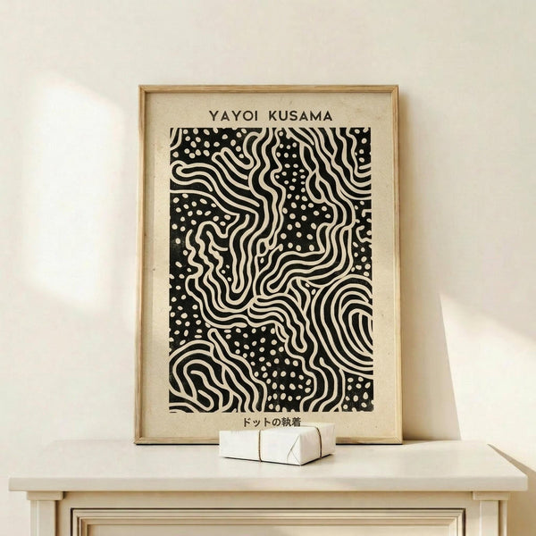 May include: Framed black and white abstract art print displayed on light wood shelf against cream wall. The artwork features flowing wavy lines interwoven with polka dot patterns in bold contrast. Natural wood frame surrounds cream-colored mat. Small white geometric objects sit on shelf beside the frame. Clean, minimalist styling with soft natural lighting casting gentle shadows.