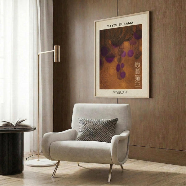 May include: Modern reading corner with beige upholstered armchair and geometric patterned pillow, featuring framed art poster with orange and brown background, purple polka dots, and Japanese text. Wood paneled wall backdrop, brass floor lamp, dark round side table with open book, and white curtains visible.