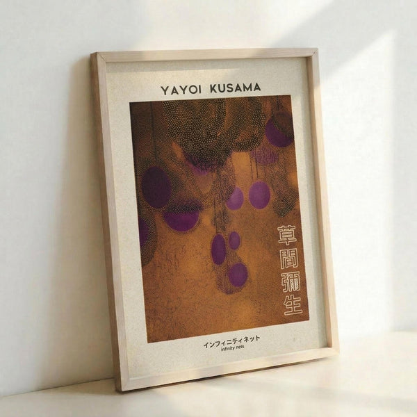 May include: Framed poster print displayed against white wall, featuring abstract artwork with orange-brown background and purple polka dots in dotted pattern style. Light wood frame with white mat, Japanese characters visible on right side, title and subtitle text at top and bottom. Natural lighting creates soft shadows on wall.