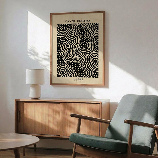 May include: Black and white abstract art print with flowing wavy lines and dotted patterns in wooden frame, displayed above mid-century modern walnut credenza with white ceramic table lamp. Sage green upholstered armchair with wooden frame sits nearby on wooden floor. Soft natural light creates shadows on white wall in minimalist living room setting.