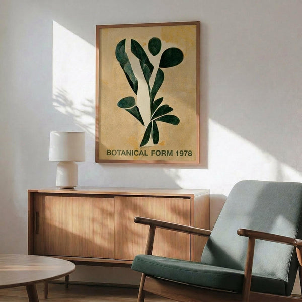 May include: Framed botanical poster with dark green leaf forms on warm beige background, displayed above wooden sideboard with table lamp in modern living room setting. Mid-century style chair with sage green upholstery sits nearby. Natural sunlight creates geometric shadows on white wall.