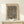 May include: Framed art print featuring abstract black wavy lines with small red-orange dots scattered throughout on cream background, displayed on light wood console table next to small white wrapped gift with evergreen sprig, against white wall with soft natural lighting
