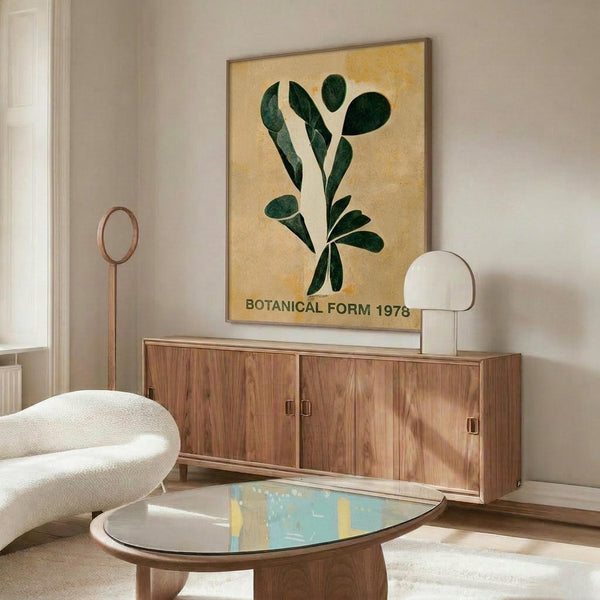 May include: Framed botanical poster with green leaves on warm yellow background mounted above mid-century walnut credenza. Modern living room setting features cream curved chair, round glass coffee table with blue accent, white sculptural lamp, and neutral walls with natural lighting.