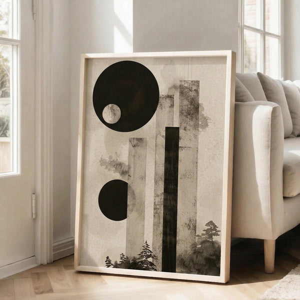 May include: Large framed abstract art print leaning against white wall next to beige armchair in bright living room. Artwork features geometric black circles, vertical rectangular shapes, and silhouetted tree forms in monochromatic palette on textured beige background with natural wood frame.