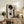 May include: Framed abstract art print featuring large black circles and geometric shapes with textured gray background and silhouetted trees, displayed on rustic wooden sideboard alongside fern plant, books, and ceramic vase in neutral-toned living room setting with beige chair