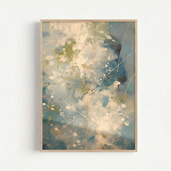 Abstract expressionist artwork in light wood frame featuring dynamic splashes of blue, green, and cream colors with white paint splatters and thin linear marks scattered across the composition. The piece has an organic, fluid quality with layered washes of color creating depth and movement. Framed print mounted on white wall.