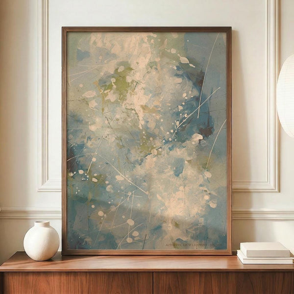 May include: Large framed abstract expressionist artwork with splattered blue, green, and cream paint, white dots, and linear scratches displayed on wooden credenza beside white ceramic vase and stacked books against cream wainscoted wall