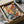 Framed abstract expressionist artwork with vibrant paint splatters in red, blue, yellow, and green against cream background, packed in cardboard shipping box with protective materials and tube packaging visible alongside