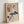 May include: Framed wall art featuring abstract geometric design with pine tree illustration, crescent moon, and grid patterns in neutral tones of beige, brown, and green. Natural wood frame displayed on white wall with soft lighting creating shadows.