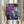 May include: Person in cream sweater holding framed abstract art print with purple, blue, and teal fluid paint splatters and white crackling lines, displayed near dried pampas grass against soft curtained window background
