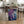 May include: Abstract artwork with purple and blue fluid paint splashes and white marble-like veining, displayed in a light wood frame leaning against a rustic wooden dining table. The poster shows flowing, organic shapes with deep violet and cobalt blue tones blending together. Kitchen setting with woven chairs, plant, and wine bottle visible in background on light wood floors.