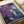 Abstract fluid art print with flowing purple, blue, and white paint creating organic shapes and delicate crackling lines throughout. The artwork features marbled textures with splashes and drips, displayed flat on white paper with a roll of paper visible in the background on a light wooden surface.
