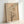 May include: Framed minimalist art print leaning against white wall showing abstract desert landscape with bare branching tree silhouette, rust orange sun, pale beige circular moon shape, and soft neutral tones on textured beige background in light wood frame