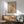 May include: Framed minimalist art print featuring bare tree silhouette against beige background with red sun and geometric circles, displayed above wood sideboard with white ceramic lamp, next to sage green mid-century armchair in sunlit room with white walls