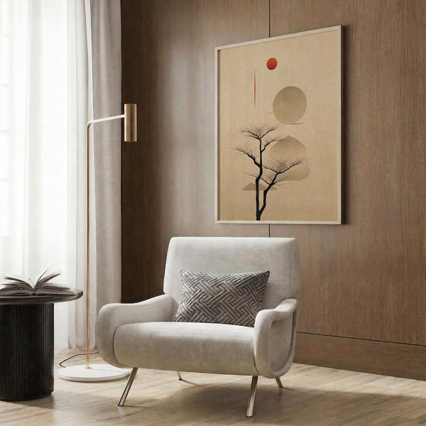 May include: Beige armchair with geometric pillow in modern living room setting. Abstract minimalist poster on wood-paneled wall features bare tree silhouette with geometric shapes - circles and rectangles in neutral tones with small red accent dot. Gold floor lamp, dark round side table with open book, and sheer curtains complete the contemporary interior scene.