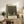 May include: Framed art print featuring a tree-lined path leading to a small building, displayed on a rustic wooden console table alongside potted fern, ceramic vase, books, and brown leather chair in a neutral-toned living room setting.