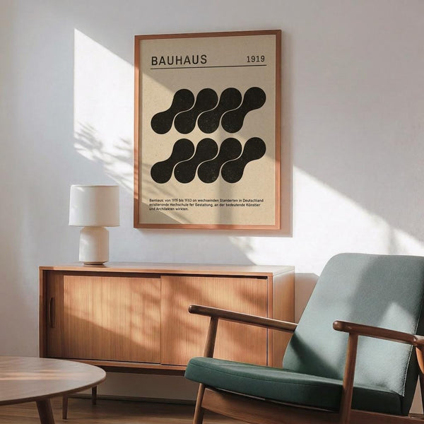 May include: Mid-century modern living room with teal upholstered armchair, wooden sideboard, white ceramic lamp, and framed Bauhaus poster on white wall. The beige poster features black abstract circular shapes arranged in two rows, dated 1919, with German text below. Sunlight streams across the scene creating geometric shadows on the minimalist interior.