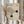 May include: Person in beige clothing holding framed Bauhaus poster with geometric design featuring curved lines forming abstract shapes and two black circles on cream background, dated 1919, with dried pampas grass visible beside them against neutral curtained backdrop