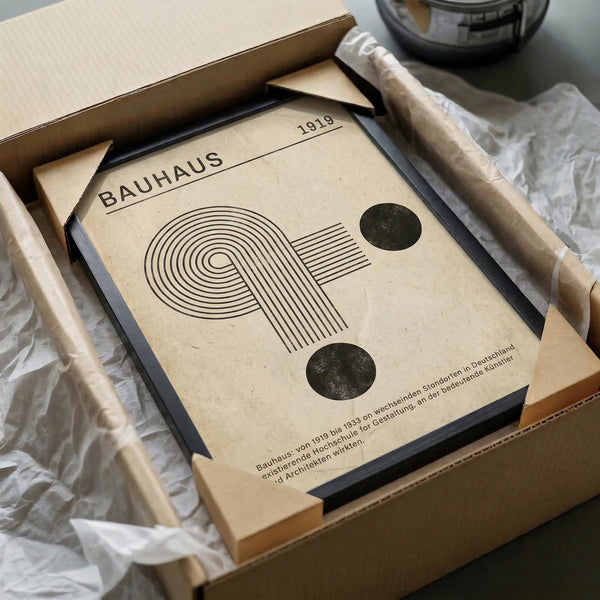 May include: Cream-colored poster with black geometric design featuring curved and straight lines forming an abstract shape, displayed in black frame inside cardboard shipping box with protective wrapping materials and wooden dowels for packaging