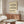 May include: Framed Bauhaus poster with wavy black lines on cream background hanging above wooden sideboard in minimalist living room with white textured chair, glass coffee table, and modern table lamp