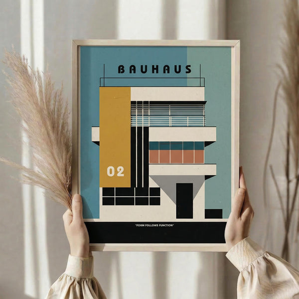 May include: Person holding framed architectural poster featuring modernist building design in geometric style with yellow, teal, coral and cream color blocks, horizontal window details, and "Form Follows Function" text at bottom. Natural lighting, pampas grass decoration visible, light wood frame against neutral interior background.