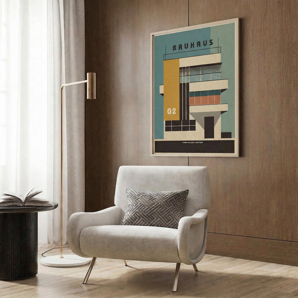 May include: Framed Bauhaus-style architectural poster featuring a modernist building in teal, yellow, orange and cream geometric shapes, displayed above a beige upholstered armchair with patterned pillow. Room has wood paneled walls, brass floor lamp, and dark round side table with open book. Poster shows clean lines and bold color blocks typical of Bauhaus design movement.