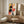 May include: Abstract geometric poster with colorful circles, rectangles and shapes in yellow, orange, red, black and blue displayed in thin frame on wooden sideboard. Modern minimalist room setting with cream textured chair, ceramic table lamp with beige shade, small wooden stool, and neutral beige walls.
