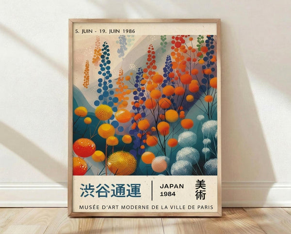May include: Framed vintage Japanese art exhibition poster featuring stylized botanical illustration with colorful dotted flowers and seed pods in orange, blue, white, and teal against cream background. Light wood frame displayed on wooden floor against white wall with soft natural lighting.