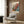 May include: Colorful botanical poster with blue, orange, and teal spherical flowers displayed on wood-paneled wall above beige upholstered armchair with geometric throw pillow. Scene includes gold floor lamp and dark round side table with open book. Poster shows exhibition details for Musée d'Art Moderne de la Ville de Paris dated June 1986.