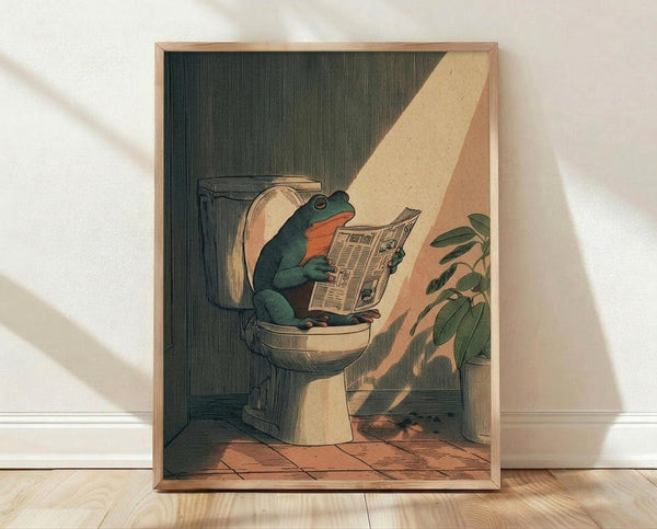 May include: Framed poster print leaning against white wall on light wood floor. Artwork shows green frog sitting on white toilet reading newspaper in bathroom setting with sunlight streaming through window, plant visible on right side. Warm color palette with earthy tones and vintage illustration style in natural wood frame.