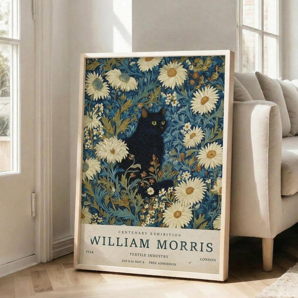 May include: Vintage-style exhibition poster featuring a black cat with yellow eyes surrounded by white daisies and blue-green foliage in William Morris decorative pattern style. Cream text area shows "CENTENARY EXHIBITION WILLIAM MORRIS 1934 TEXTILE INDUSTRY LONDON JAN 6 to MAY 6 FREE ADMISSION." Framed print leans against white wall next to beige upholstered chair in bright, airy room with hardwood floors and large windows.
