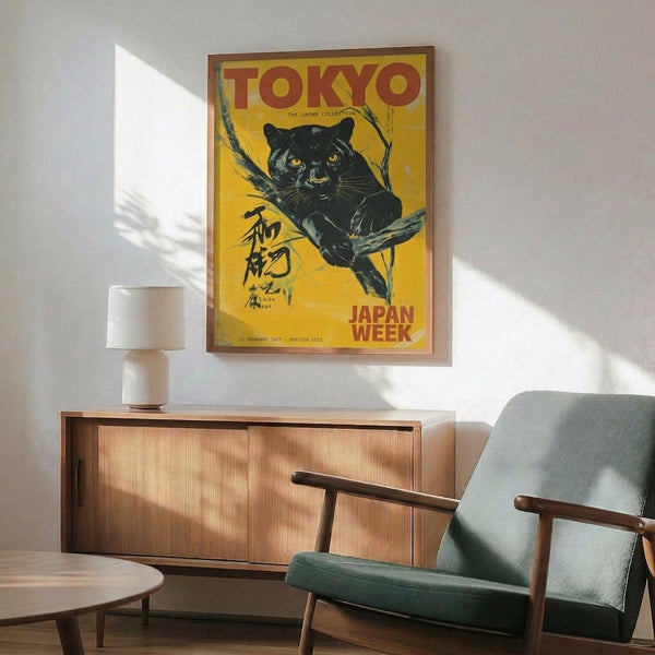May include: Vintage-style poster featuring a black panther perched on a tree branch against a yellow background, with "TOKYO" in red letters and Japanese characters below, displayed in a wooden frame above a mid-century modern credenza. Room setting shows a mint green upholstered chair with wooden arms, small white table lamp, and round wooden side table, all bathed in natural sunlight creating geometric shadows on white walls.