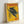 May include: Vintage-style poster with yellow background featuring black panther with golden eyes perched on tree branch, red "TOKYO" text at top, Japanese characters on left side, "JAPAN WEEK" in red at bottom right, dated February 1977, displayed in light wood frame leaning against white wall