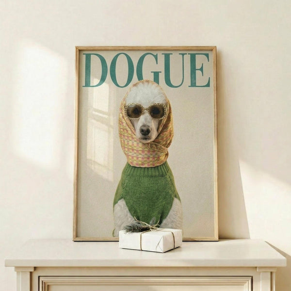 May include: Framed poster showing a white poodle wearing round sunglasses, green knit sweater, and colorful striped headscarf styled like a vintage fashion magazine cover with "DOGUE" in teal letters at top. Light wood frame sits on pale wooden surface next to small white wrapped gift box with natural twine and sprig. Cream colored wall background with soft natural lighting.