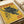 Vintage-style poster with yellow background featuring a black panther with golden eyes positioned on tree branches. Red text reads "TOKYO" at top and "JAPAN WEEK" at bottom right. Japanese characters appear in black ink on lower left. Date "12 FEBRUARY 1977 - EDITION 5/12" printed at bottom. Poster appears aged with weathered texture and is photographed flat against white paper with rolled paper tubes visible in background.