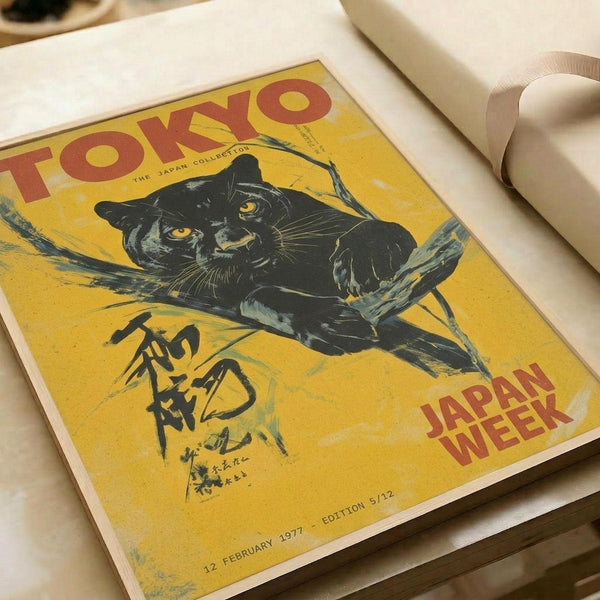 Vintage-style poster with yellow background featuring a black panther with golden eyes positioned on tree branches. Red text reads "TOKYO" at top and "JAPAN WEEK" at bottom right. Japanese characters appear in black ink on lower left. Date "12 FEBRUARY 1977 - EDITION 5/12" printed at bottom. Poster appears aged with weathered texture and is photographed flat against white paper with rolled paper tubes visible in background.