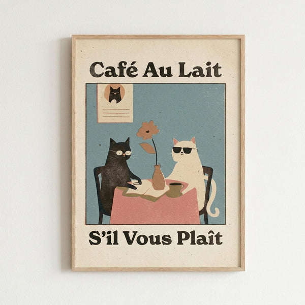 May include: Framed vintage-style poster with cream background and light wood frame hanging on white wall. Features two cats sitting at cafe table with pink tablecloth - black cat wearing glasses on left, white cat with sunglasses on right. Brown vase with flower centerpiece between them. Blue-green background with small framed cat portrait on wall. French text "Café Au Lait" above and "S'il Vous Plaît" below illustration in bold black lettering.