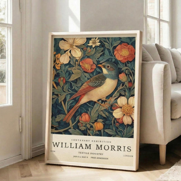 May include: Framed vintage-style poster with colorful bird and floral design in warm tones of orange, cream, and teal, leaning against white wall next to beige upholstered chair in bright room with large windows and natural light streaming across wooden floors.