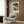 May include: Vintage William Morris poster featuring two white swans among cream and coral flowers on dark green background, displayed in light wood frame on wood paneled wall above beige upholstered armchair with geometric patterned pillow, brass floor lamp and side table with open book nearby