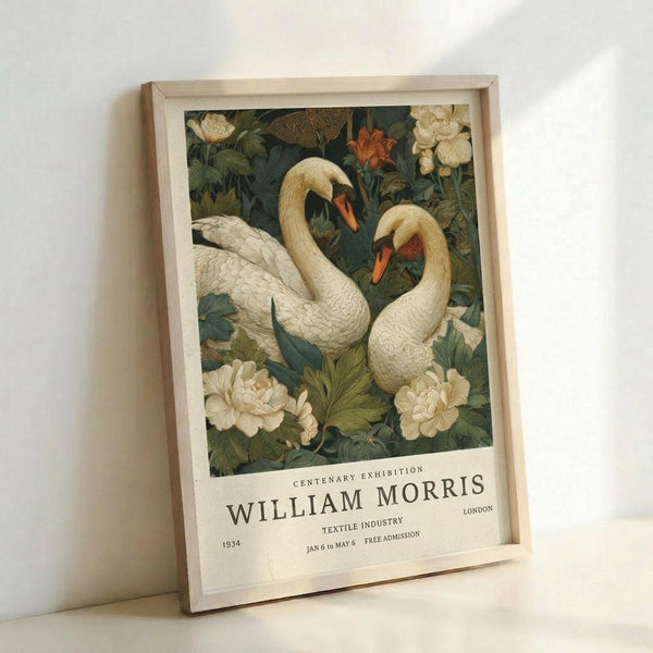 May include: Framed vintage exhibition poster featuring two white swans with orange beaks swimming among cream and coral flowers on a dark teal background. The poster shows "William Morris Centenary Exhibition" text at bottom. Light wood frame leans against white wall, showing detailed botanical textile design pattern with rich colors and ornate Victorian Arts and Crafts style illustration.
