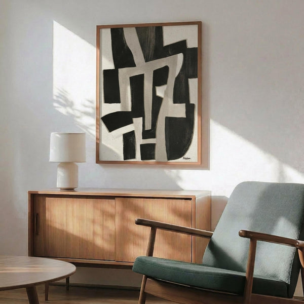 May include: Abstract black and white geometric artwork in wooden frame hanging above mid-century modern walnut credenza with table lamp. Sage green upholstered armchair with wooden arms sits nearby in bright, minimalist room with white walls and natural sunlight streaming across the space.