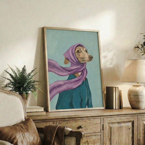 May include: Framed painting of an Italian Greyhound wearing a flowing purple headscarf and teal garment against a soft blue-green background, displayed on a rustic wooden console table alongside ferns, books, and ceramic pottery in a cozy living room setting with neutral tones and natural lighting.