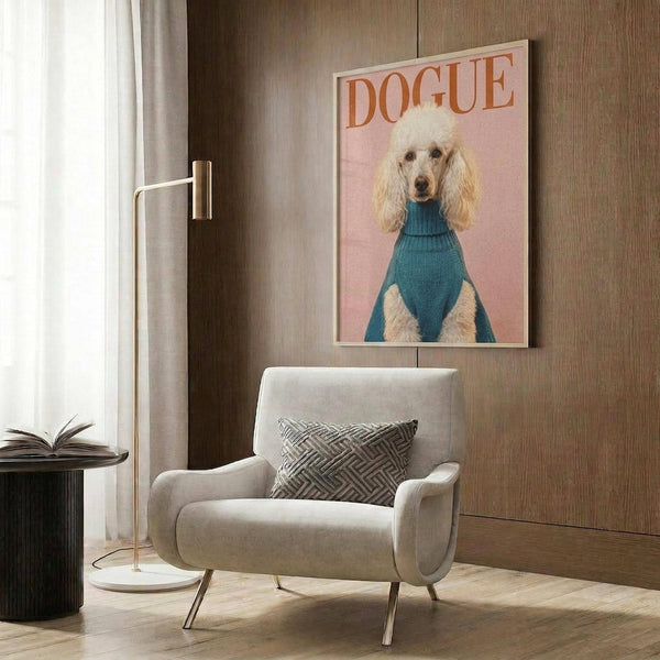 May include: Framed poster print on wood-paneled wall above beige upholstered armchair with geometric pillow. Artwork shows white poodle wearing teal blue turtleneck sweater against soft pink background with "DOGUE" text at top. Modern living room setting with brass floor lamp, side table with open book, and natural lighting from window with curtains.