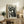 May include: Black and white vintage-style poster featuring three stylized cats with bold geometric patterns and polka dot background, displayed in light wood frame on rustic wooden sideboard. Room setting shows beige armchair, potted fern, ceramic vases, and books creating cozy living space with neutral tones.