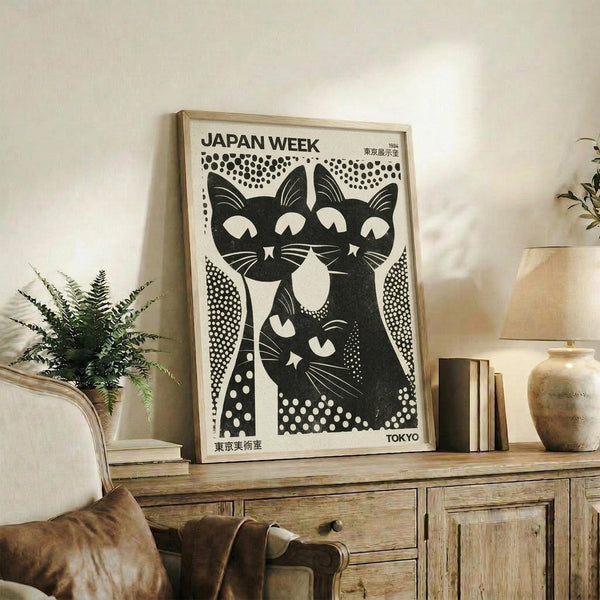 May include: Black and white vintage-style poster featuring three stylized cats with bold geometric patterns and polka dot background, displayed in light wood frame on rustic wooden sideboard. Room setting shows beige armchair, potted fern, ceramic vases, and books creating cozy living space with neutral tones.