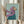 May include: Hands holding a framed painting of a tan Italian Greyhound wearing a flowing purple headscarf and teal garment against a mint green background. The artwork is in a light wood frame, held alongside dried pampas grass stems in a bright room with white curtains and neutral walls.